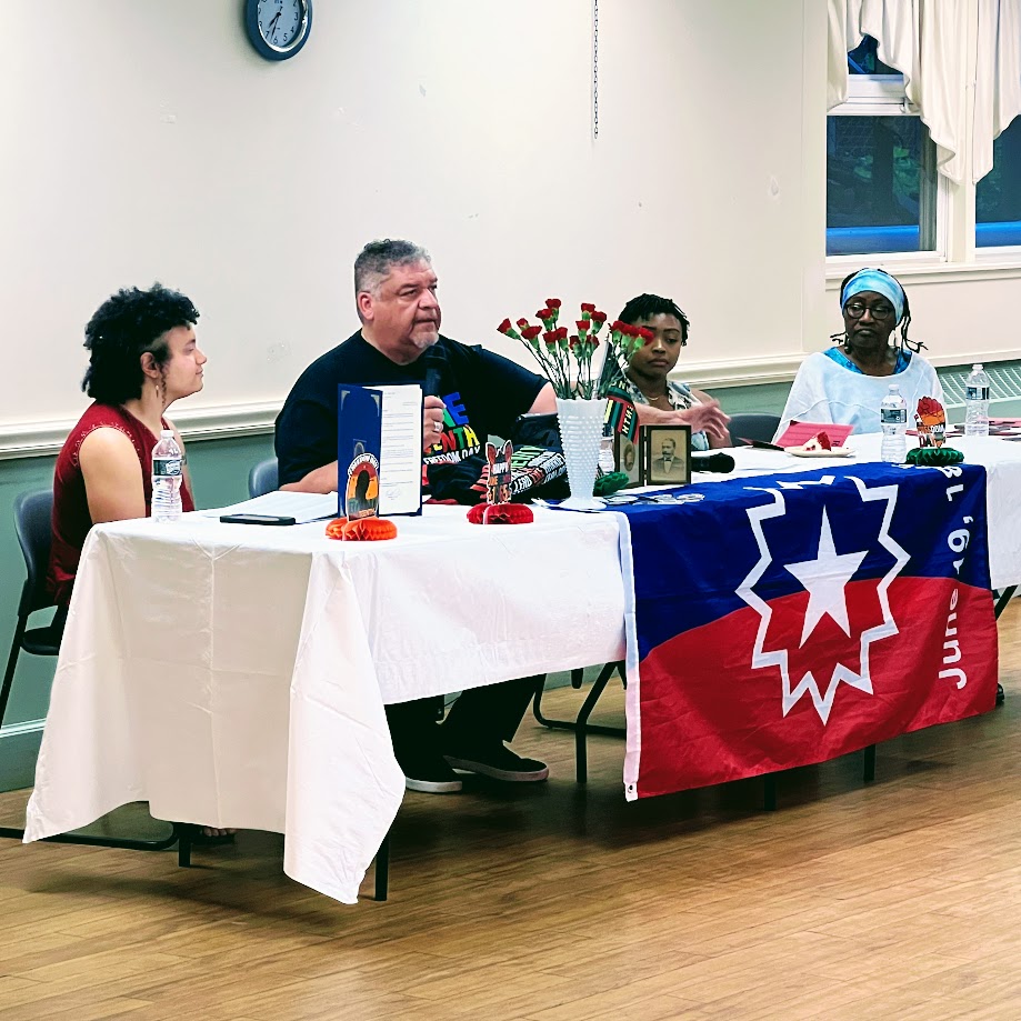 Juneteenth event showing four participants sitting at a table and giving a presentation