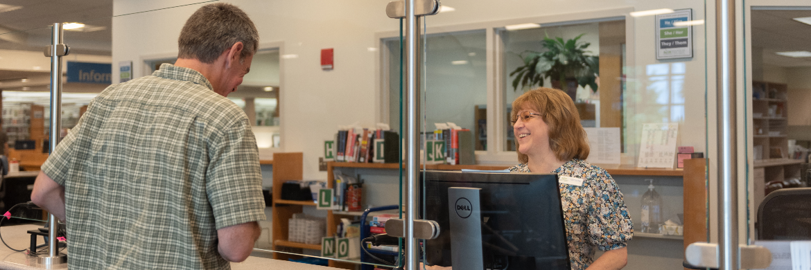 Staff member smiling as they check out items for a happy library user