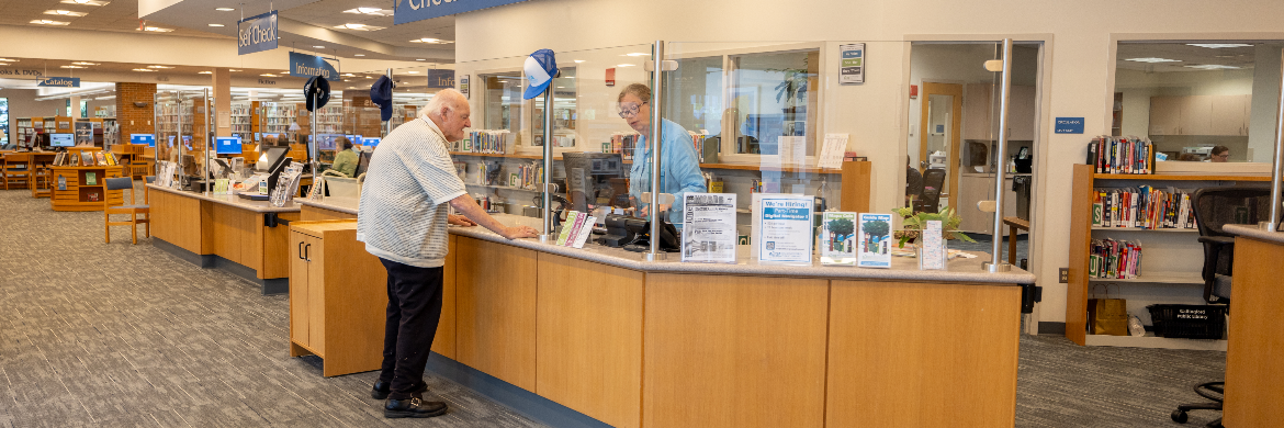 Older gentleman checks out materials from library staff at the Borrowing Desk