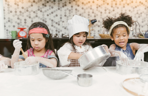 Three happy children cooking at a table and making a mess