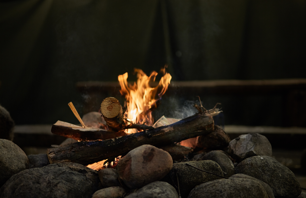 Small fire on logs atop smooth rocks. Wooden bench seating blurry in the background.