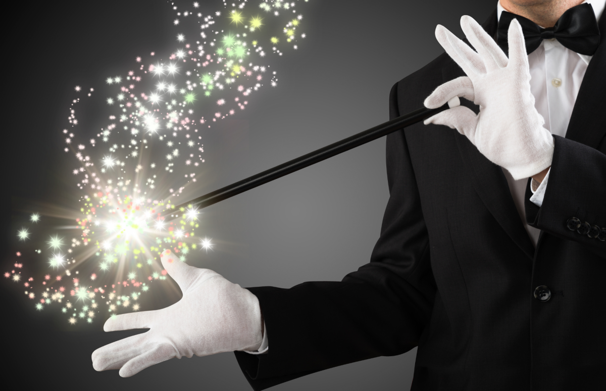 Magician's hands waving wand at a hat with light glowing out of it