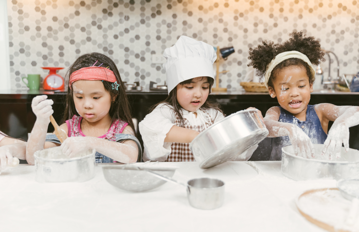 Three happy children cooking at a table and making a mess