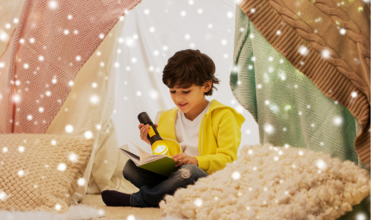 A boy reading by flashlight in a blanket fort with snowflakes falling down